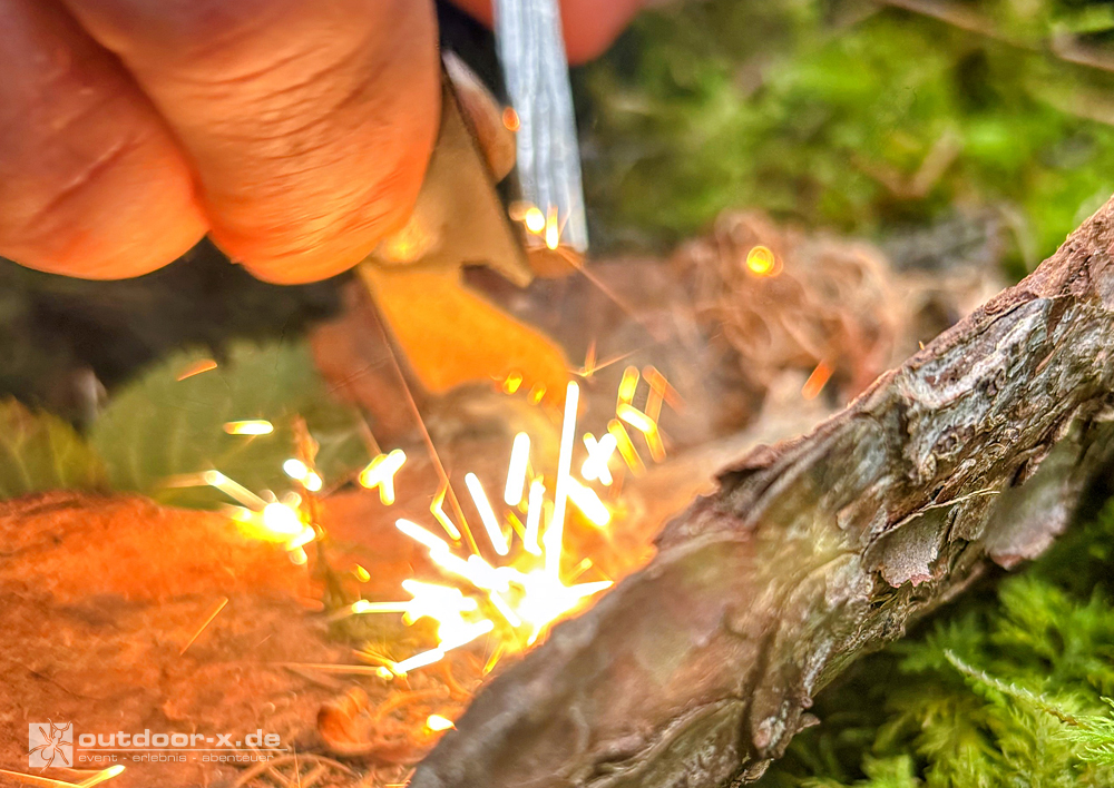Outdoor-X Academy Outdoor-Abenteuer für Vater und Kind: Nahaufnahme eines Feuerstahls, dessen Funken beim Entzünden von Zunder auf trockenes Brennmaterial sprühen.